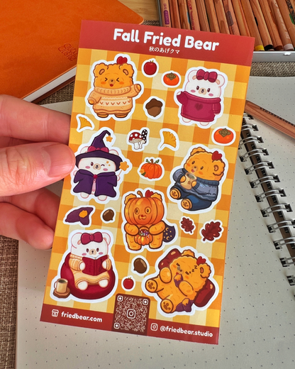 Hand holding the Fall Fried Bear sticker sheet with pumpkins, sweaters and a witch hat over a notebook