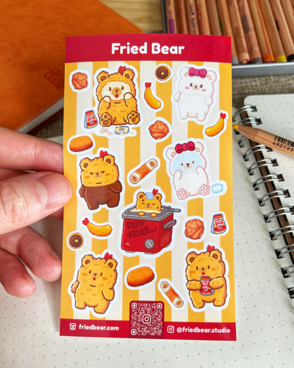 Hand holding the Fried Bear sticker sheet with Fried Bear, Tofu Bear and fried foods over a notebook