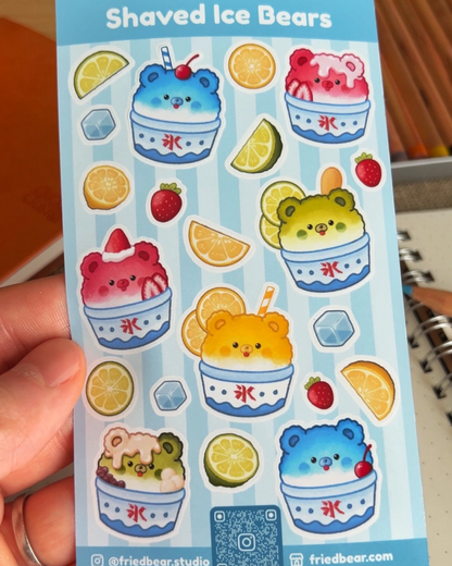 Hand holding the Shaved Ice Bears sticker sheet with bears in kakigori cups and fruit over a notebook