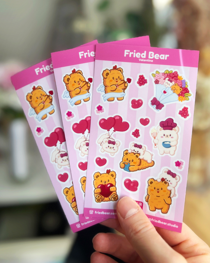 Three Fried Bear Valentine sticker sheets with hearts, balloons and a bouquet fanned out in a hand